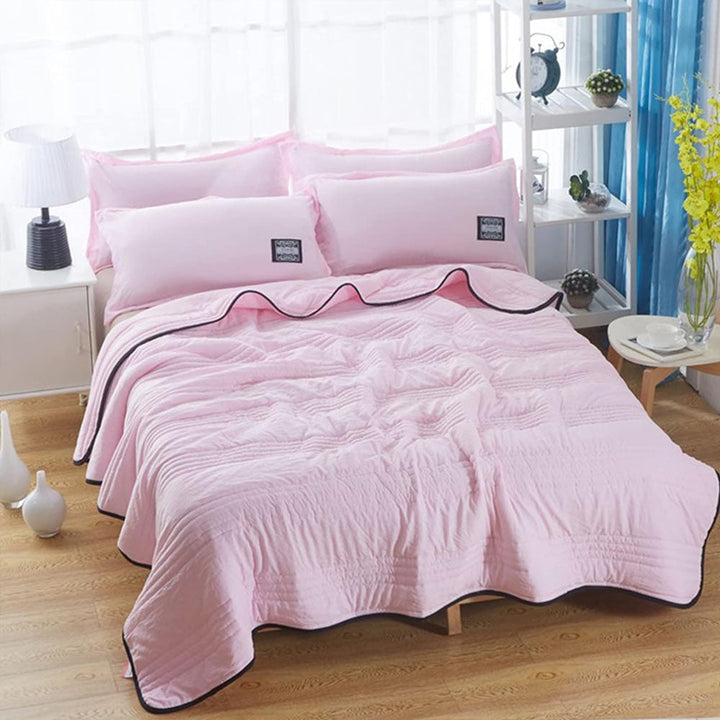 Pink cooling blanket with black trim, folded on a bed with pink pillows.