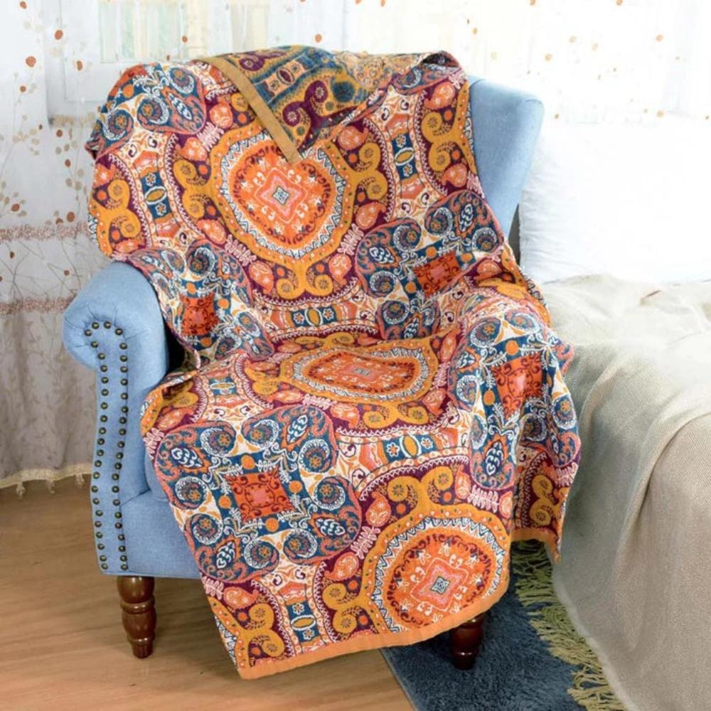 A blue armchair draped with a colorful boho-style cotton bath towel featuring geometric and floral patterns in orange, yellow, and blue.