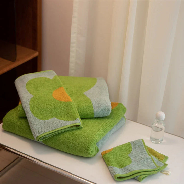 Green and light blue floral cotton bath towels folded on a white surface with a small glass bottle.
