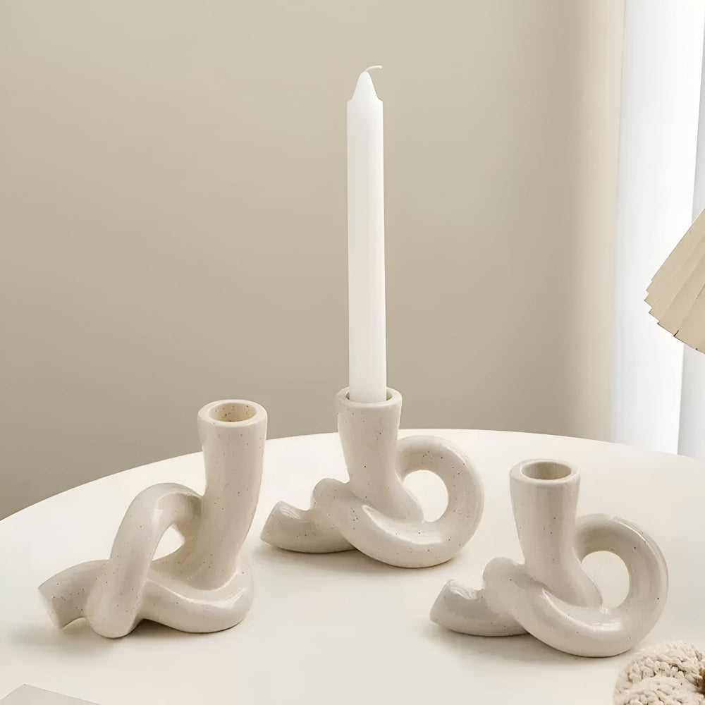 Three cream-colored ceramic candle holders with a knotted, minimalist design on a white table.