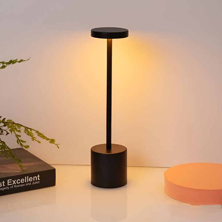 Black cordless table lamp with a round top and cylindrical base, emitting warm light.