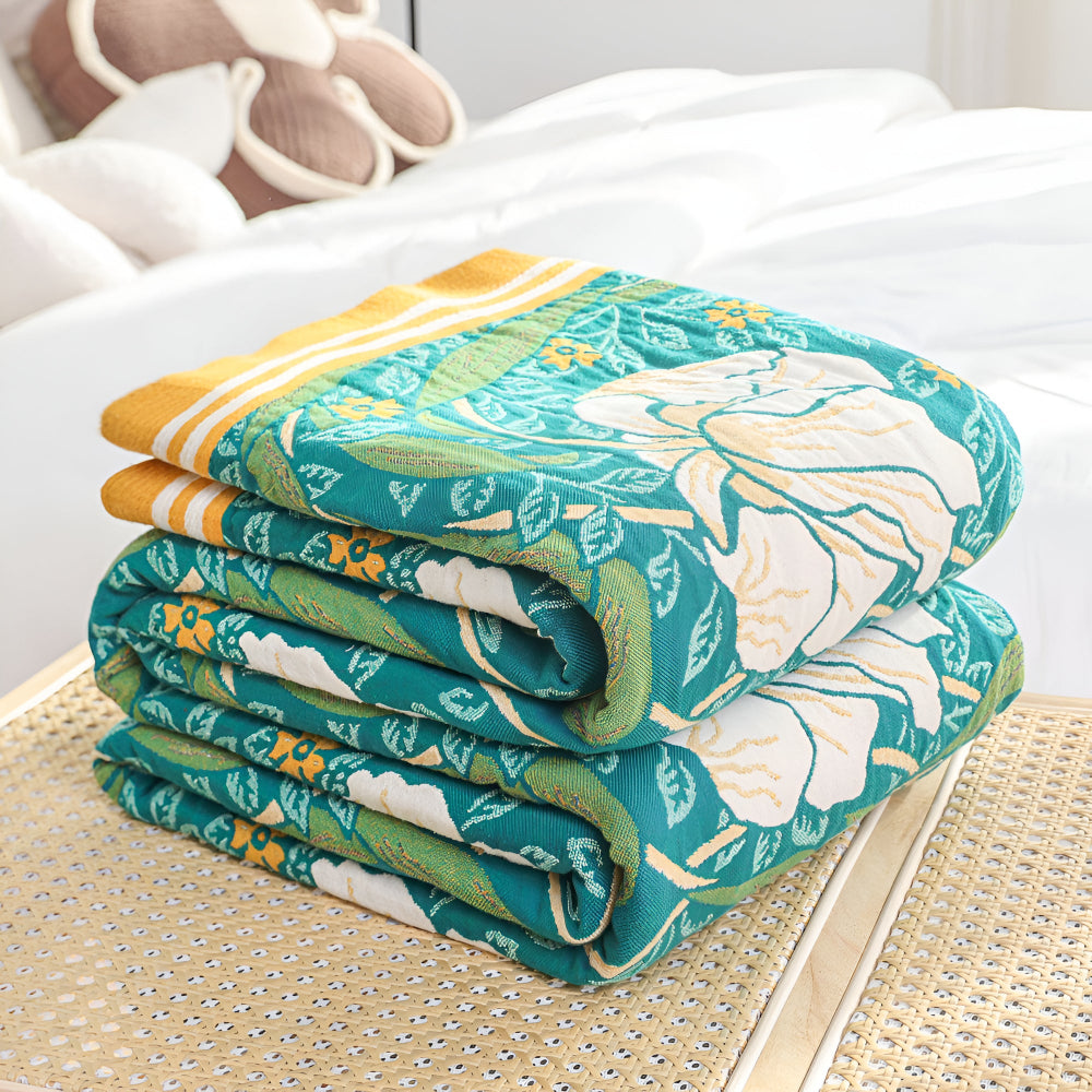 Stack of folded green botanical bloom cotton blankets with yellow trim.