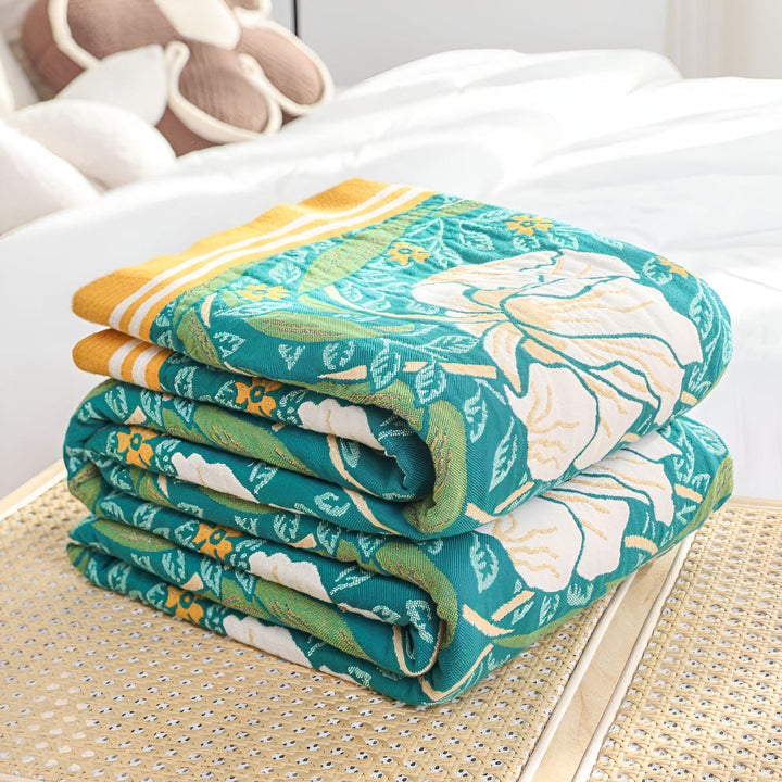Stack of folded green botanical bloom cotton blankets with yellow trim.
