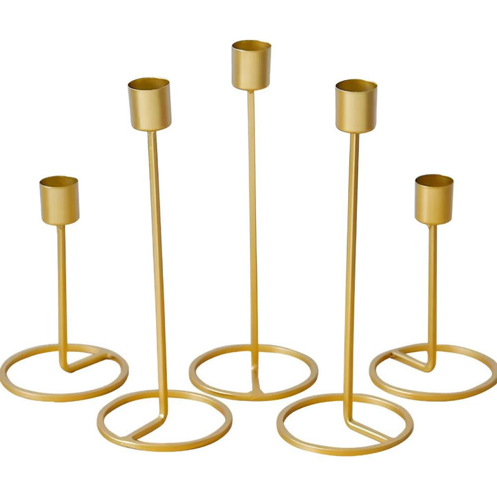 Five gold metal candle holders of varying heights with round bases.