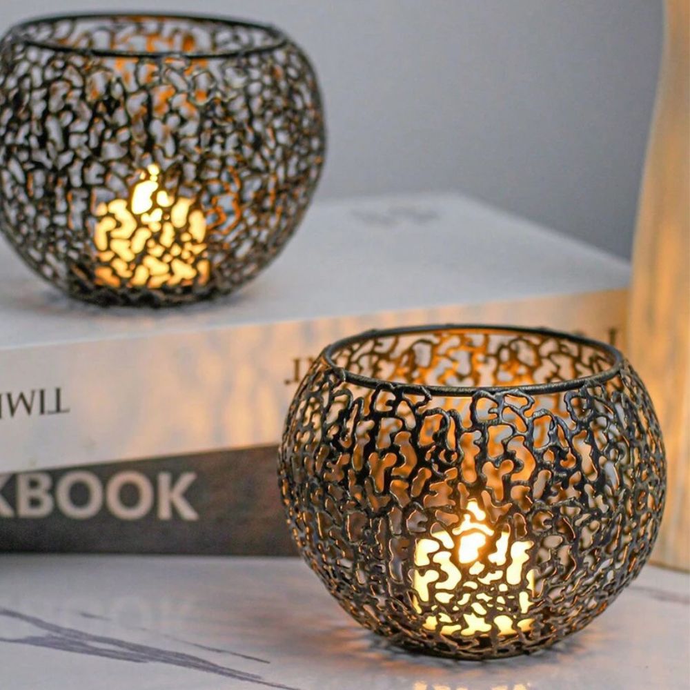 Two black geometric iron tealight holders with a sphere design, one in the foreground and one in the background, both lit with candles.