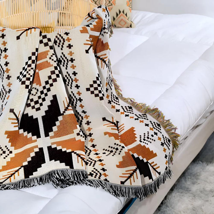 Moroccan boho picnic mat with geometric patterns in brown, black, and white, draped on a white bed.