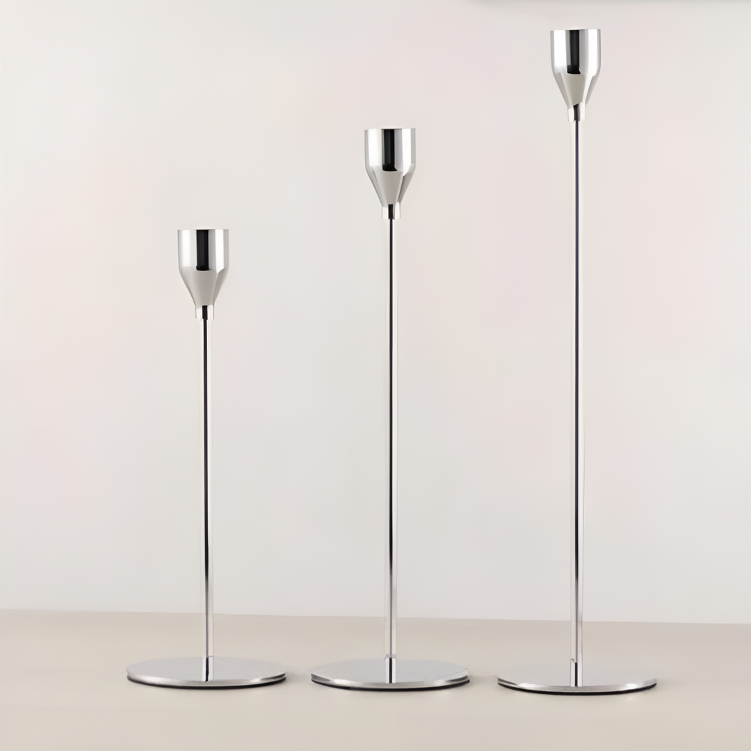 Three brushed metal taper candle holders of varying heights on a light surface.