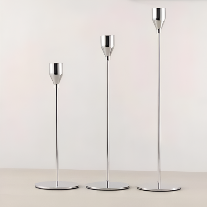 Three brushed metal taper candle holders of varying heights on a light surface.