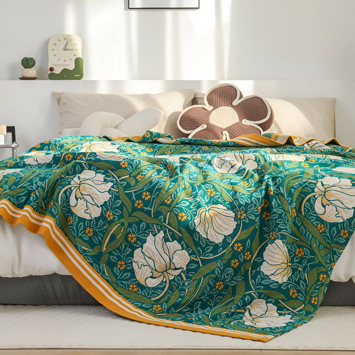 Green botanical bloom cotton blanket with white flowers and yellow accents, draped on a bed.