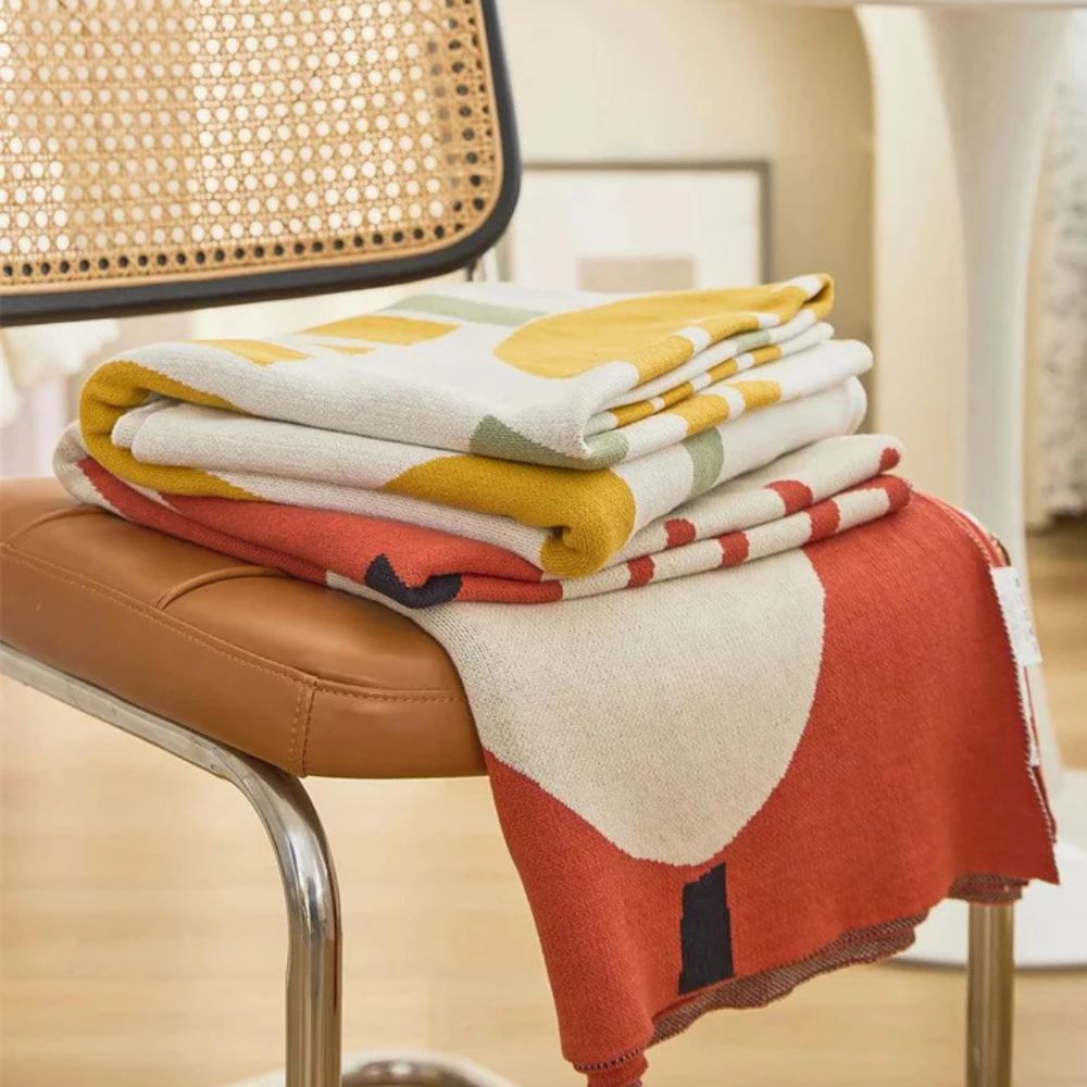 A stack of folded knitted blankets with floral and striped patterns in yellow, red, and cream colors.