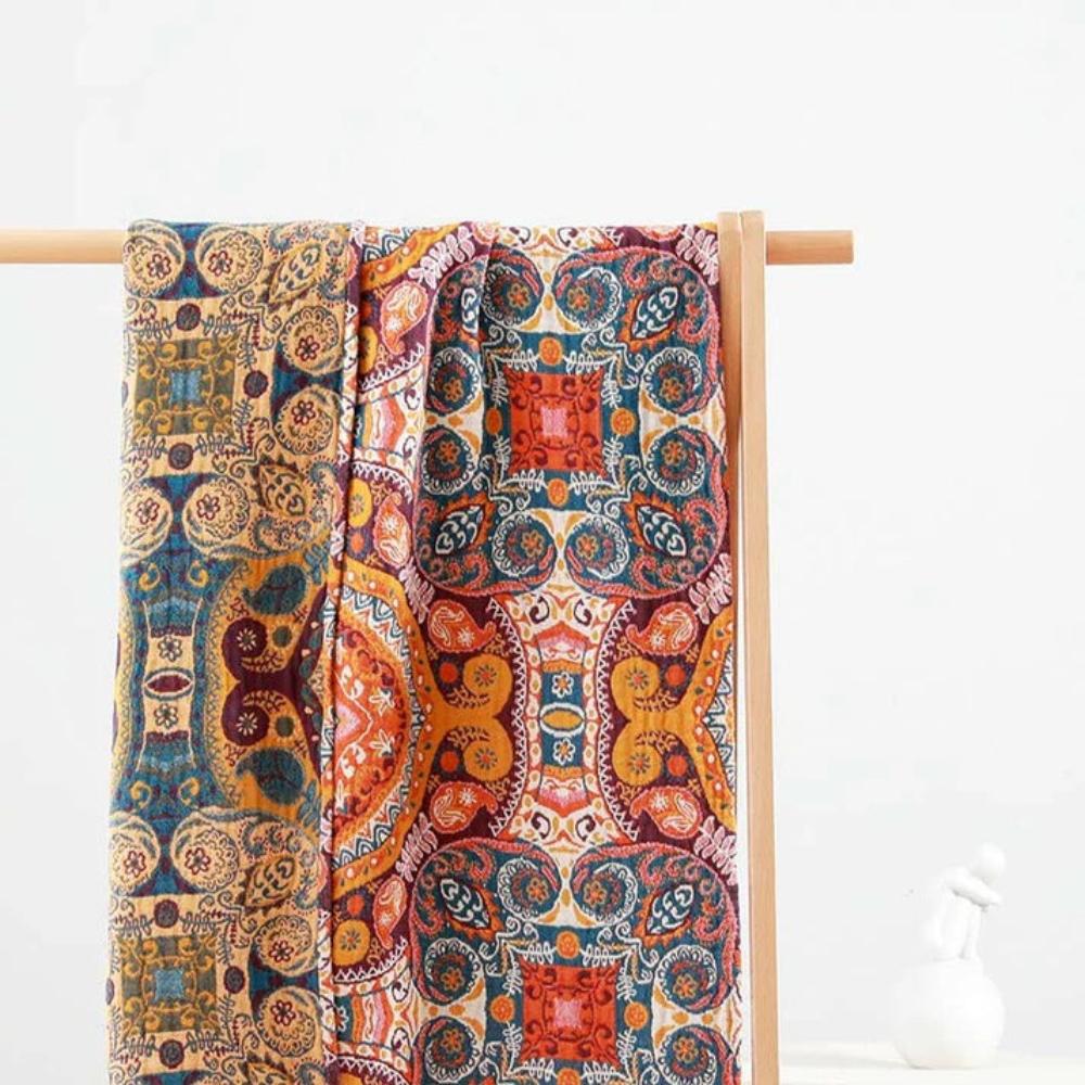 Two cotton bath towels with colorful boho geometric and floral patterns hanging on a wooden rack.