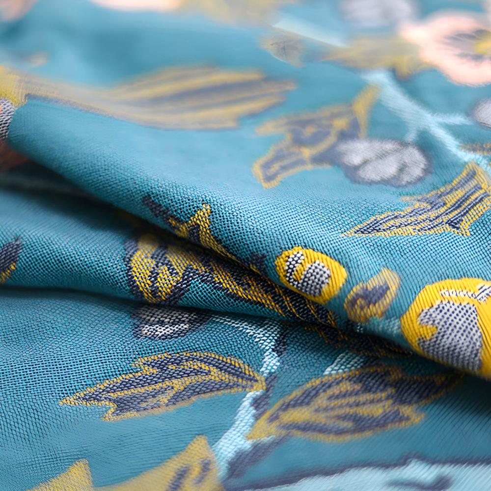 Close-up of a teal cotton bath towel featuring a reversible yellow and blue hibiscus floral pattern.