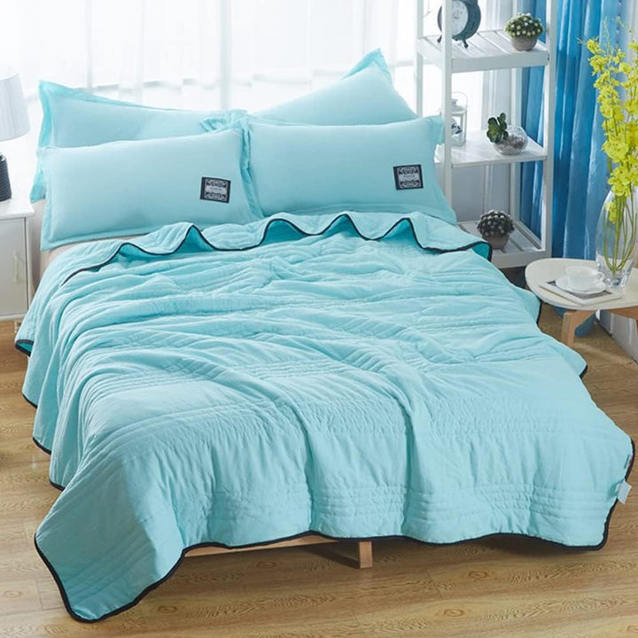 Light blue EverChill Ice Cooling Blanket with black trim, folded on a bed with matching pillows.