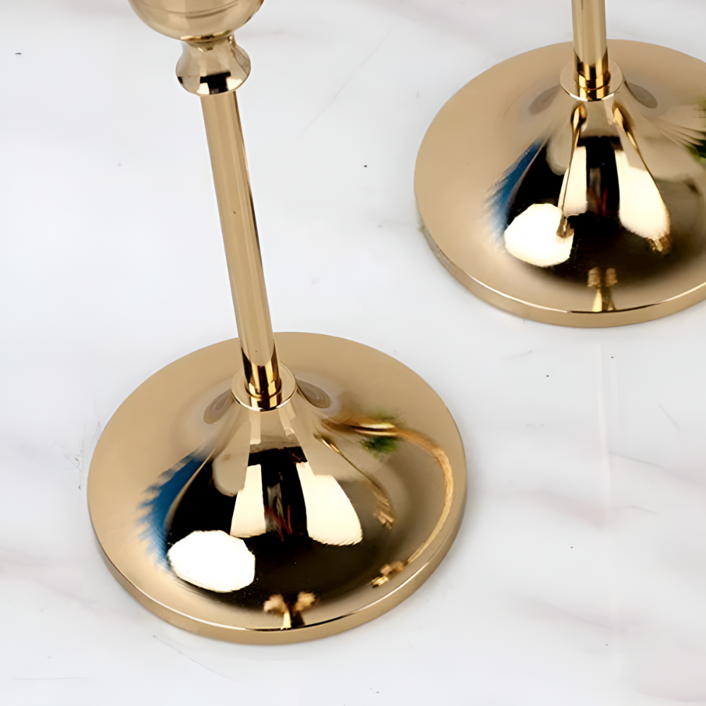 Two gold taper candle holders with round bases on a marble surface.
