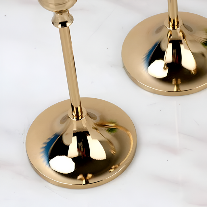 Two gold taper candle holders with round bases on a marble surface.