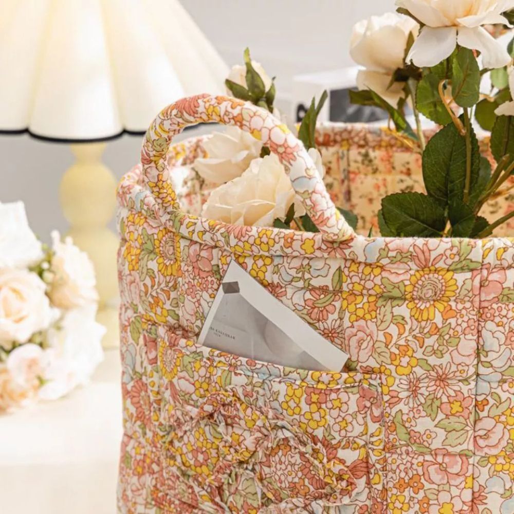 Delicate floral canvas storage basket with a pocket holding a small booklet, filled with light-colored roses.