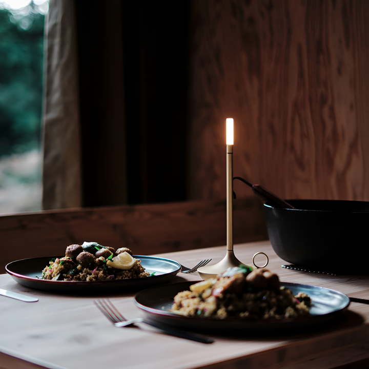 Portable aluminum table lamp with USB-C charging, casting a warm glow over a meal.