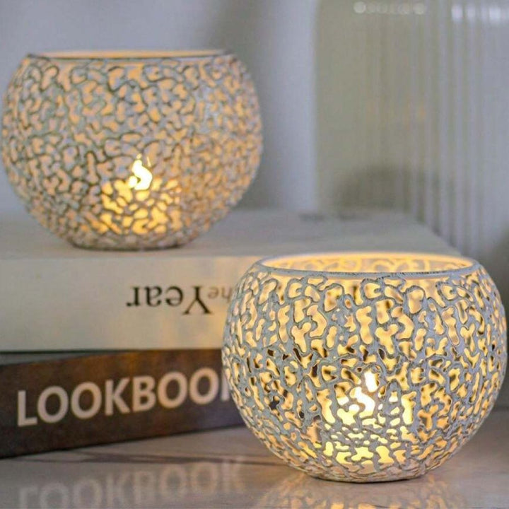 Two spherical iron tealight holders with a geometric cut-out design, one in front of the other, with lit candles inside.