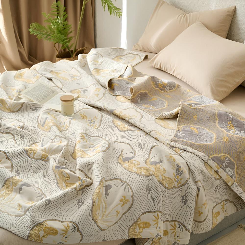 Reversible blanket with a white, gold, and grey cloud and wave pattern, draped on a bed with pillows.