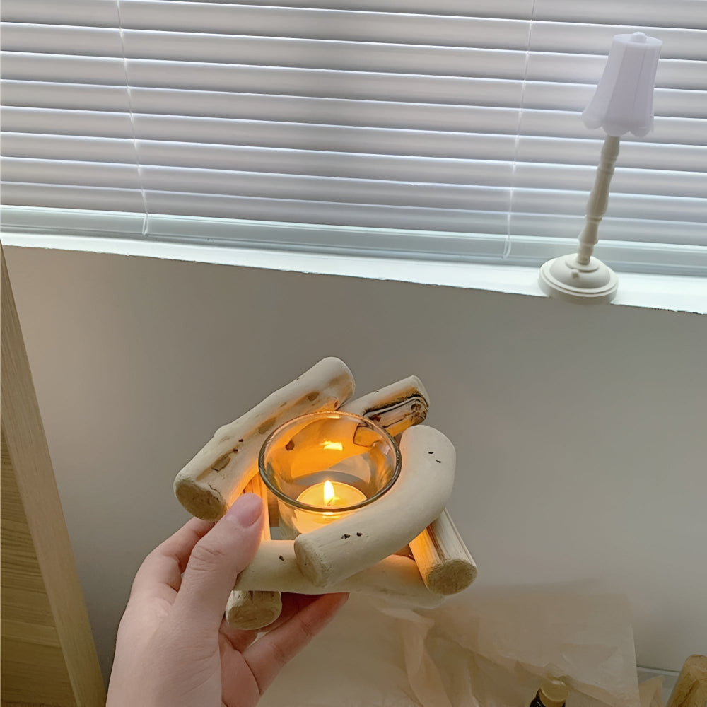 A hand holds a driftwood tealight holder with a lit candle inside, placed on a windowsill.