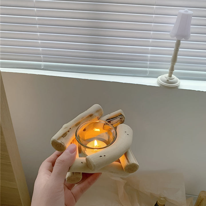 A hand holds a driftwood tealight holder with a lit candle inside, placed on a windowsill.