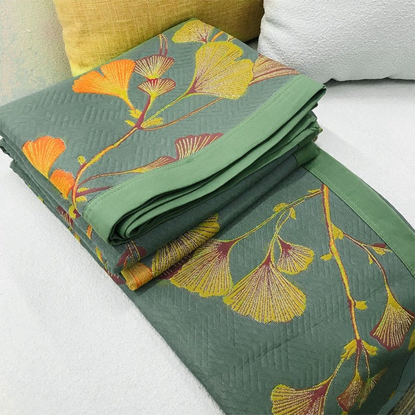 Green reversible coverlet with a jacquard weave and a pattern of orange, yellow, and red ginkgo leaves.