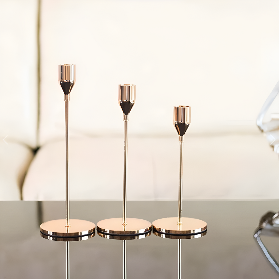 Set of three brushed metal taper candle holders with different heights on a reflective surface.
