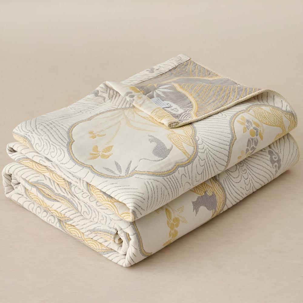 A folded blanket with a white, gold, and gray oriental bird and floral pattern.
