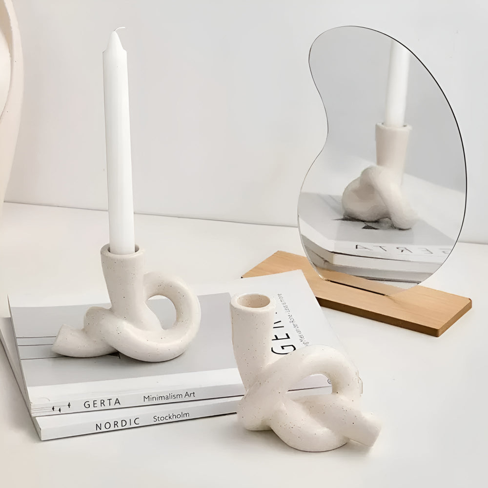 Two white ceramic knot candle holders, one with a white candle, on a stack of books.