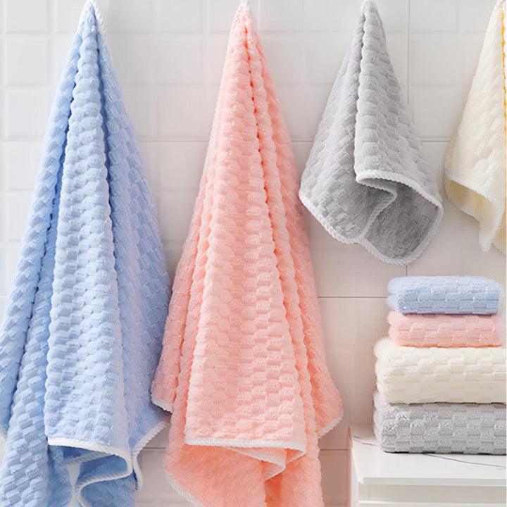 A set of soft fleece towels in blue, pink, gray, and yellow hanging on a tiled wall and stacked on a shelf.
