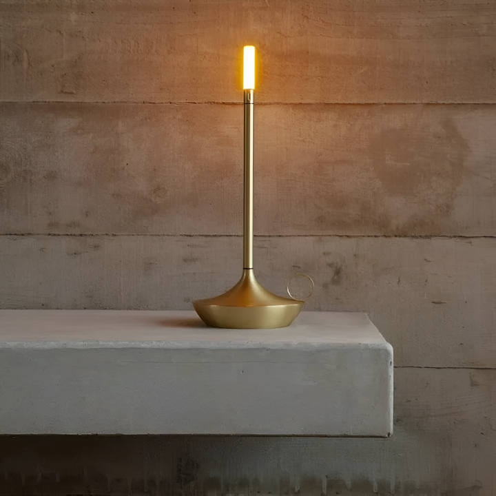 Gold portable table lamp with a cylindrical light and a flared base, placed on a concrete surface.