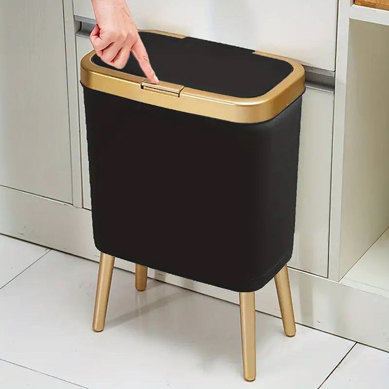 Black 15L elevated trash can with gold trim and legs, lid being opened by a finger.