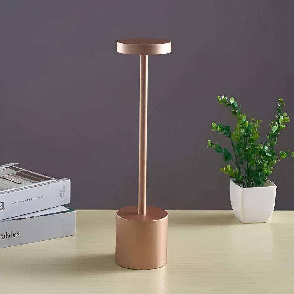 Gold cordless table lamp with a round base and a slender stem topped with a light.