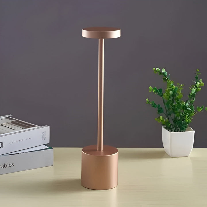 Gold cordless table lamp with a round base and a slender stem topped with a light.