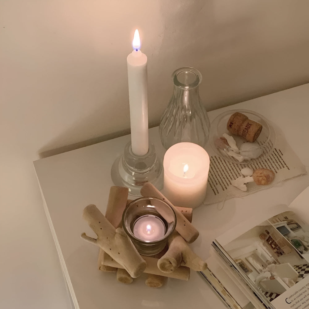 A driftwood tealight holder with a lit candle inside, next to other candles and a book.