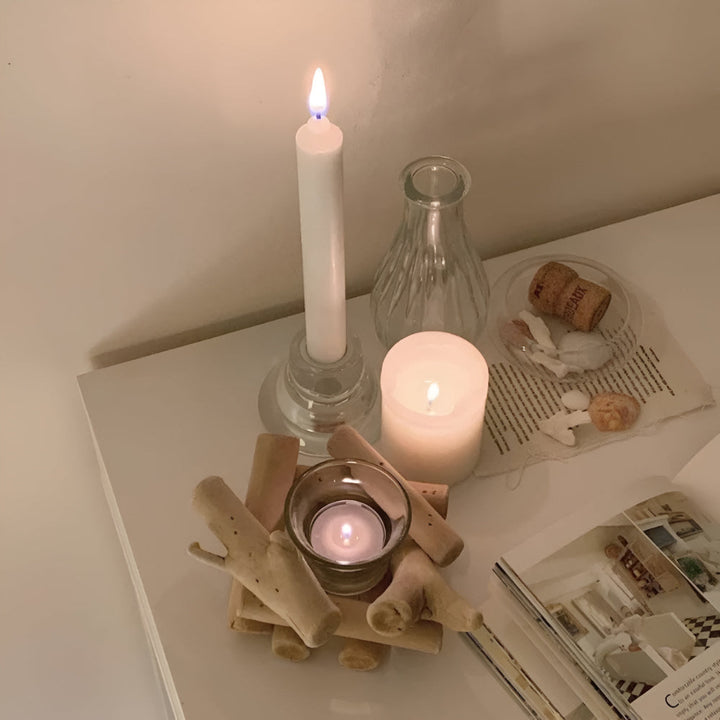 A driftwood tealight holder with a lit candle inside, next to other candles and a book.