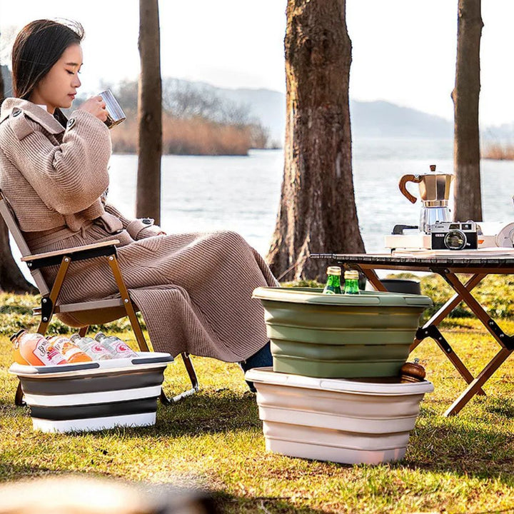 Collapsible storage baskets in green and beige, one filled with drinks, beside a woman sitting outdoors.