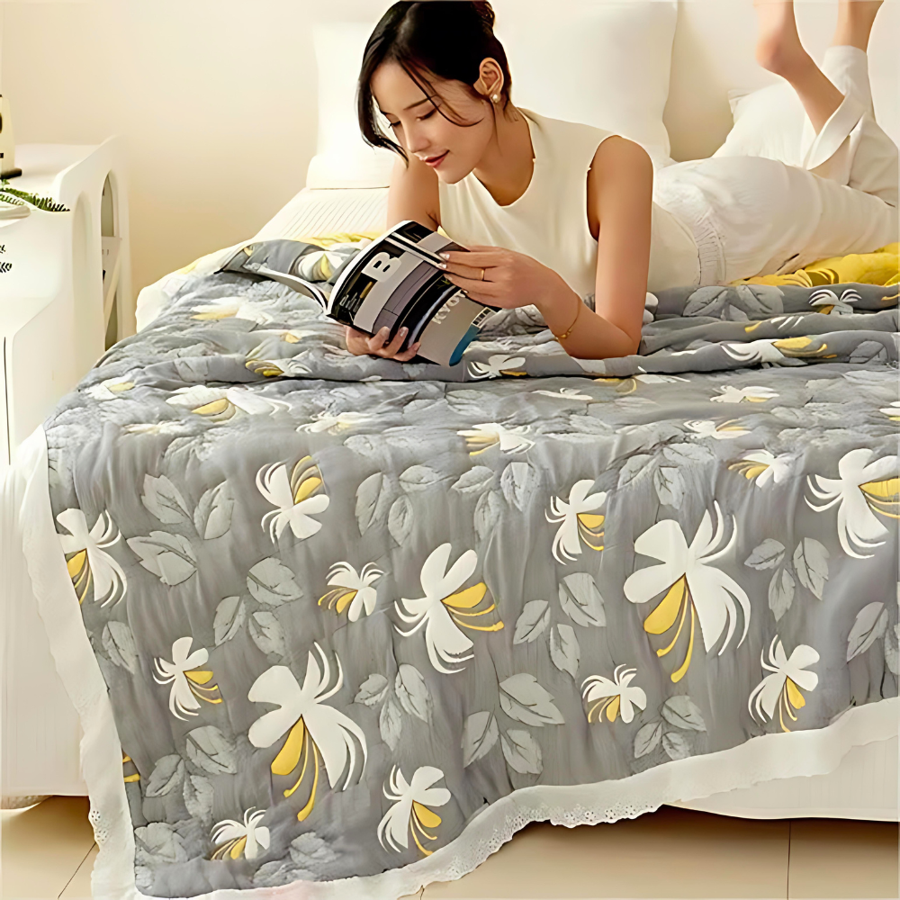 Woman reading on a bed covered with a grey blanket featuring a white and yellow floral pattern.