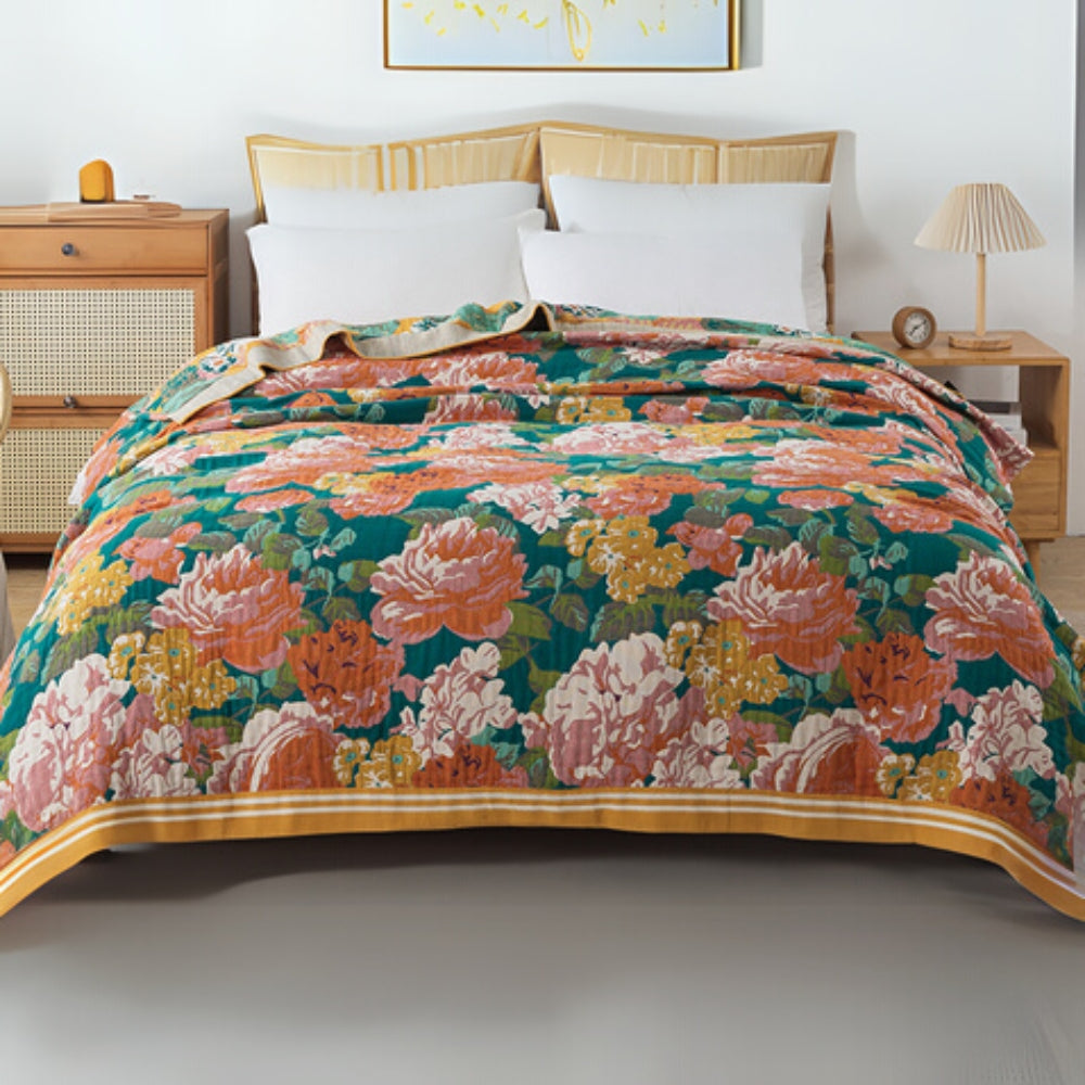 A teal cotton blanket with a large floral pattern in pink, orange, and yellow, draped over a bed.