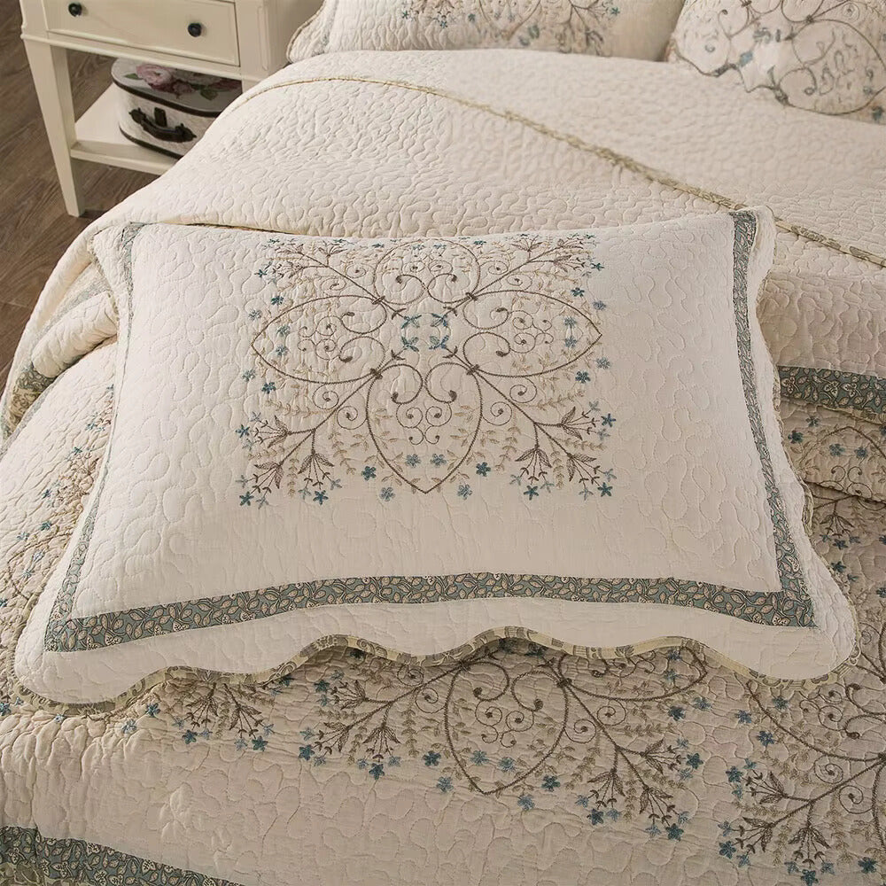 Cream coverlet with embroidered floral medallion pillow and scalloped edge.