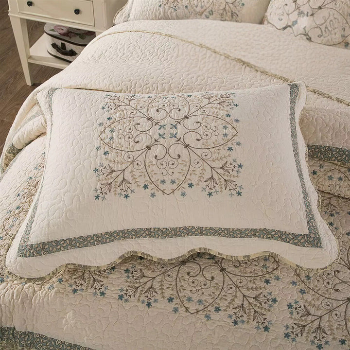 Cream coverlet with embroidered floral medallion pillow and scalloped edge.