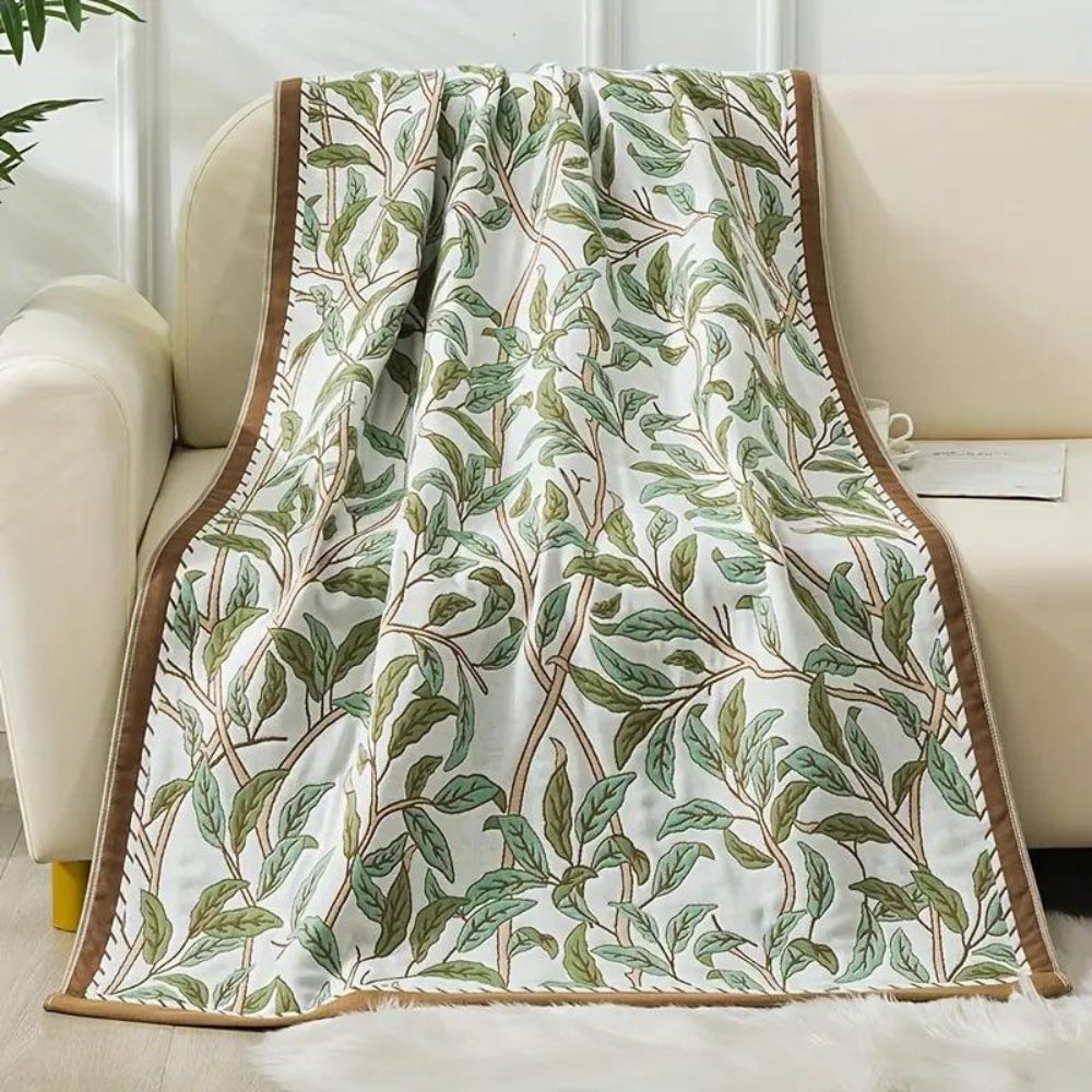White cotton bath towel with a brown border and a repeating pattern of green leaves and brown branches.