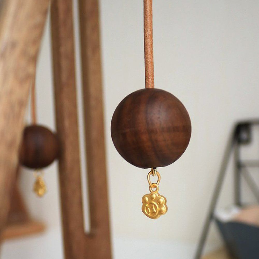 Wooden ball with a gold charm hanging from a leather cord, part of a paper roll stand.