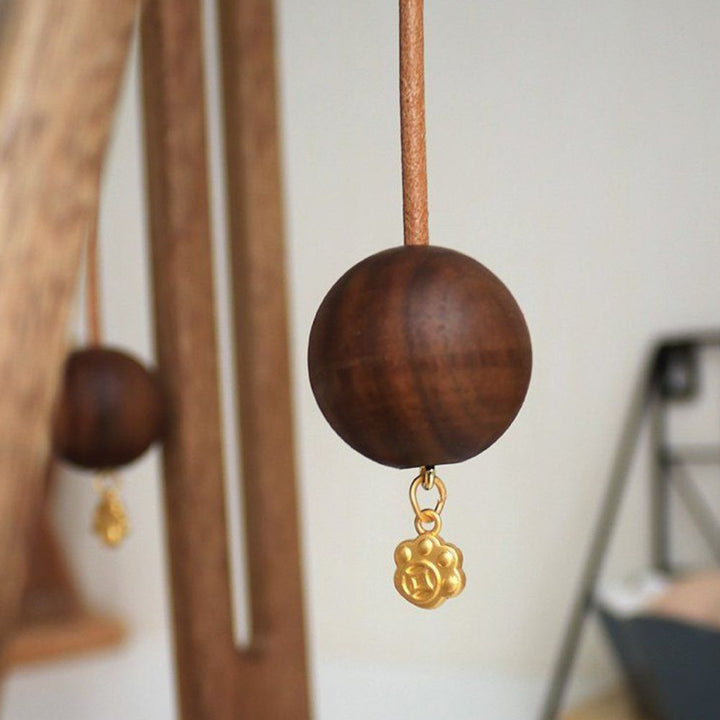 Wooden ball with a gold charm hanging from a leather cord, part of a paper roll stand.