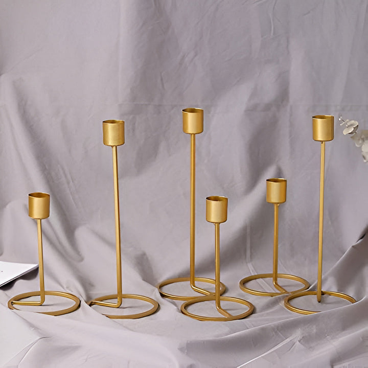 Six golden metal candle holders of varying heights with circular bases.
