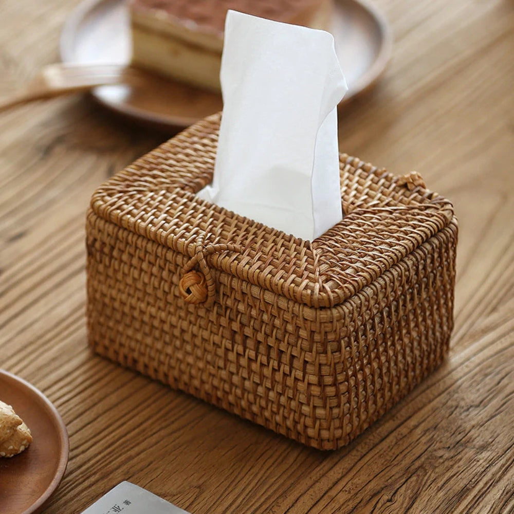 Handwoven rattan tissue box with white tissues emerging from the top and a loop closure on the front.
