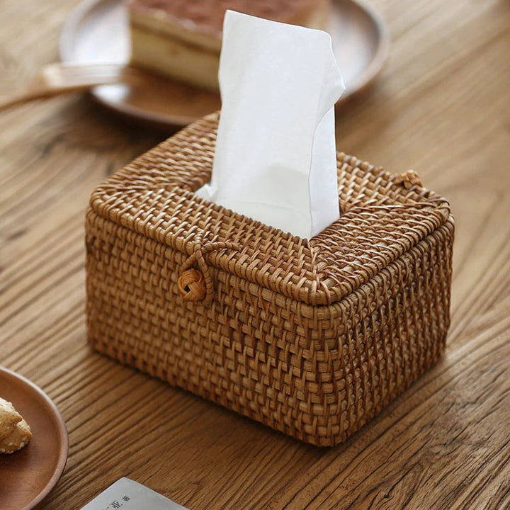Handwoven rattan tissue box with white tissues emerging from the top and a loop closure on the front.