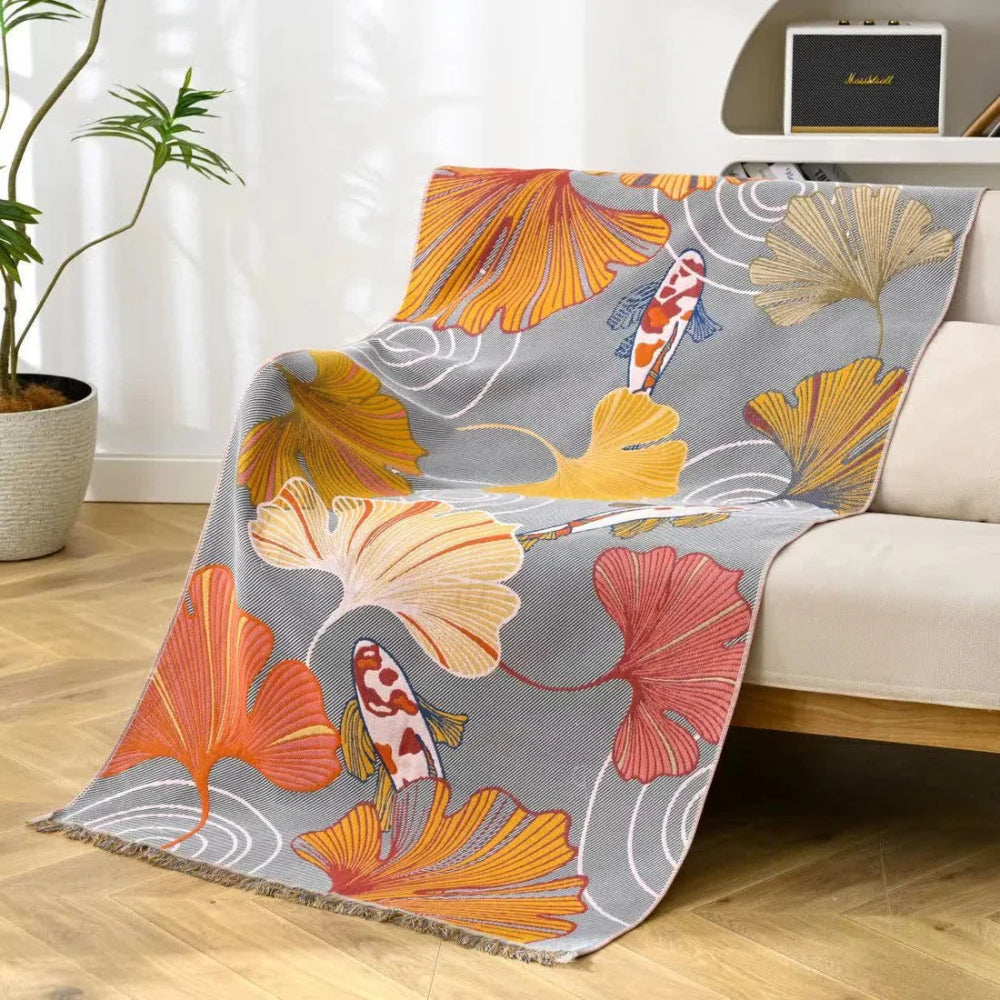 A grey throw blanket with a pattern of koi fish and ginkgo leaves in orange, yellow, and red.