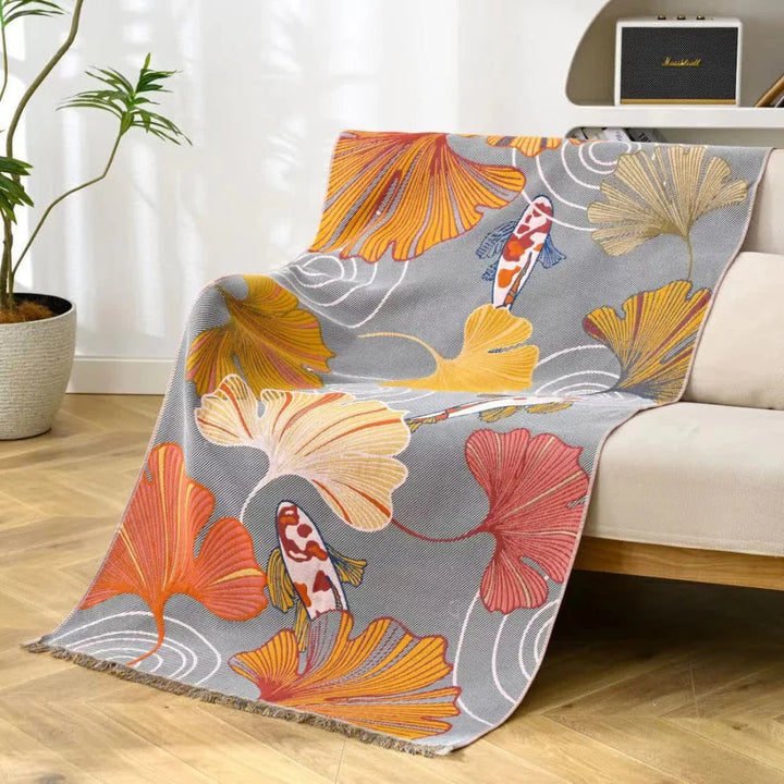 A grey throw blanket with a pattern of koi fish and ginkgo leaves in orange, yellow, and red.