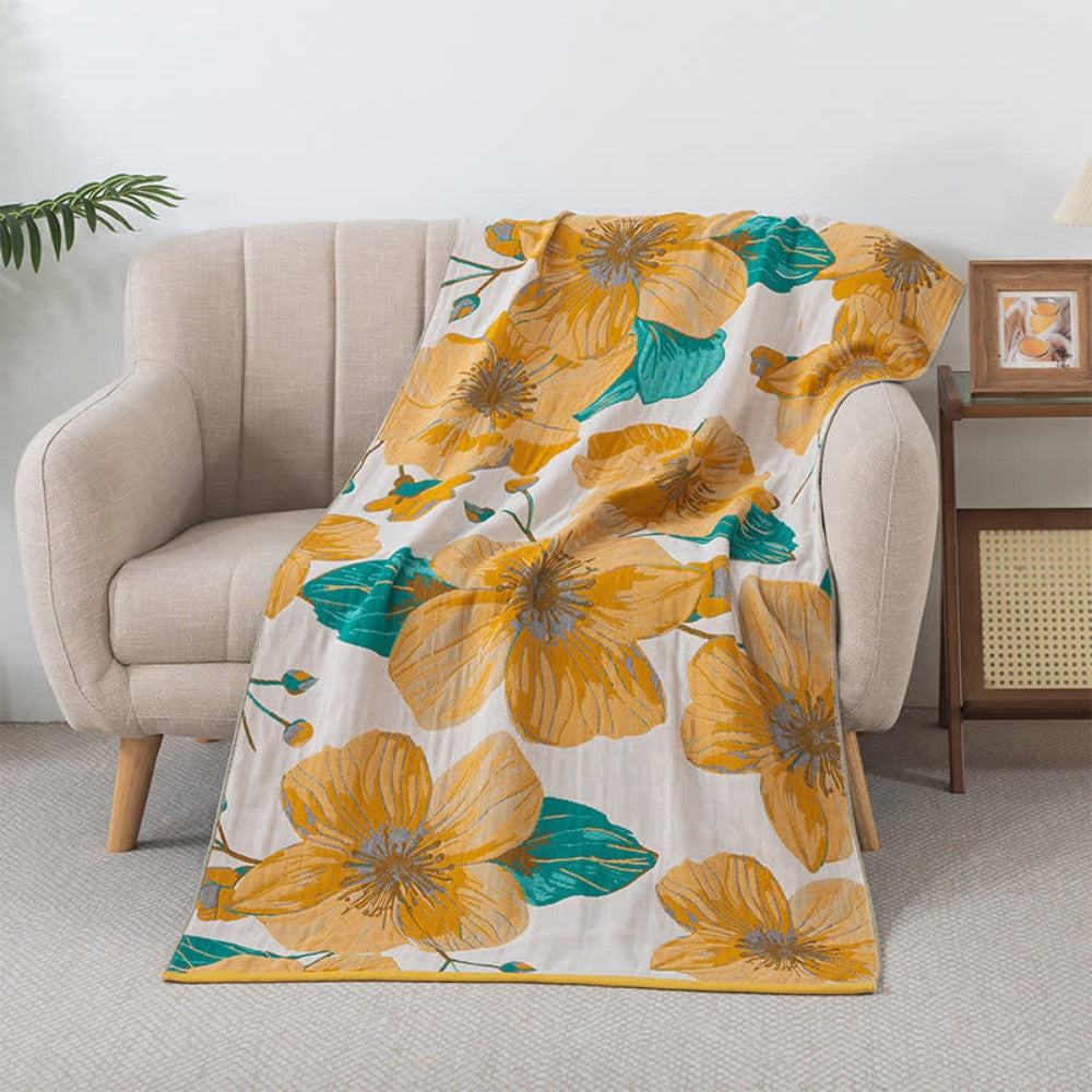 A soft, 100% cotton bath towel with a large yellow floral print and teal leaves, draped over a light-colored armchair.